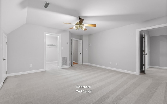 unfurnished bedroom featuring light colored carpet, a ceiling fan, a walk in closet, baseboards, and vaulted ceiling