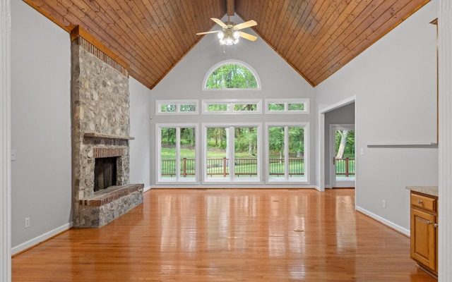 unfurnished living room with ceiling fan, a stone fireplace, light wood finished floors, high vaulted ceiling, and baseboards