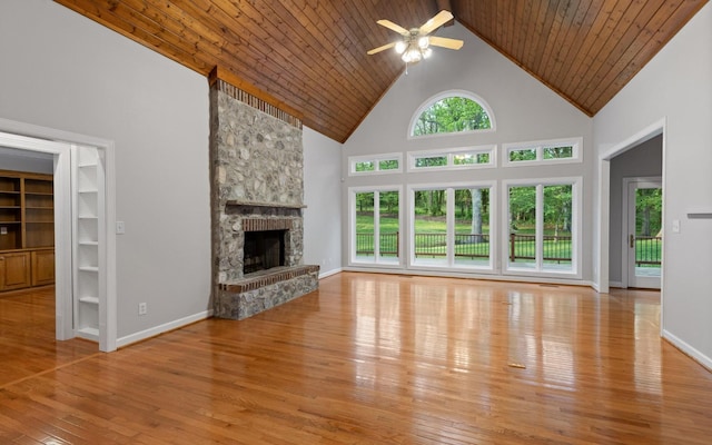 unfurnished living room featuring ceiling fan, hardwood / wood-style floors, high vaulted ceiling, a stone fireplace, and baseboards