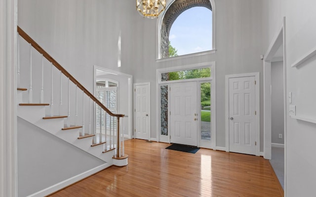 entryway with a high ceiling, a chandelier, wood finished floors, stairs, and baseboards