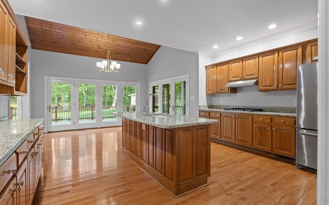 kitchen featuring stainless steel appliances, a sink, under cabinet range hood, brown cabinetry, and a chandelier