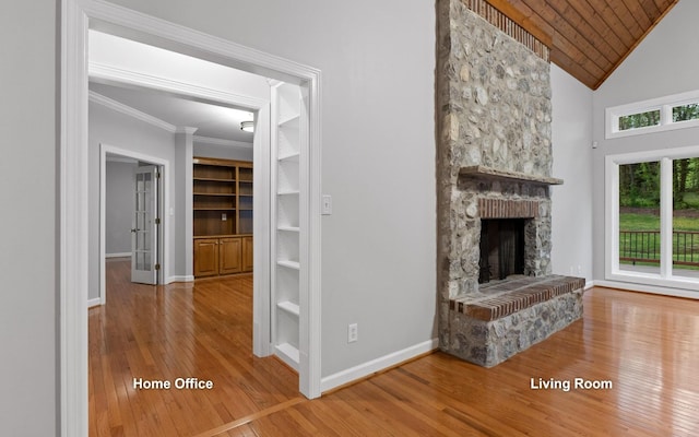 unfurnished living room featuring hardwood / wood-style flooring, a stone fireplace, baseboards, ornamental molding, and built in shelves