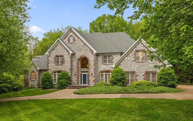 traditional-style house with a front yard, a shingled roof, and stone siding
