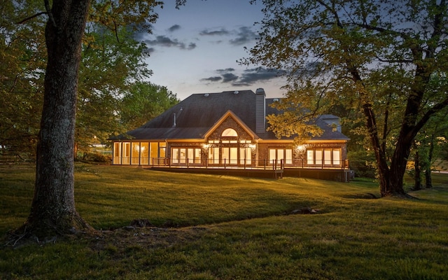 back of house at dusk with a lawn, a deck, and french doors