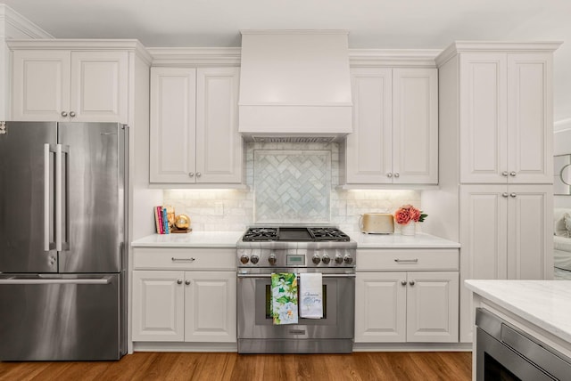 kitchen featuring stainless steel appliances, premium range hood, light wood-style flooring, decorative backsplash, and white cabinetry