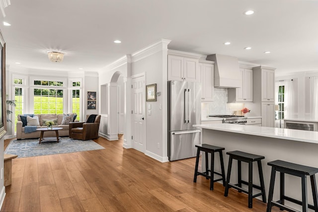 kitchen featuring high quality fridge, premium range hood, light countertops, a breakfast bar area, and plenty of natural light