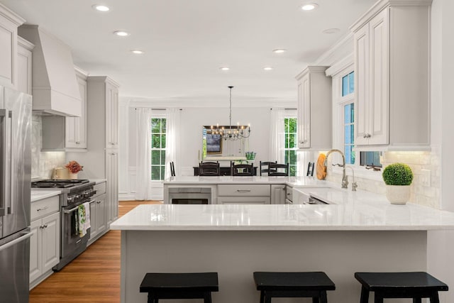 kitchen featuring appliances with stainless steel finishes, a peninsula, custom exhaust hood, recessed lighting, and a sink
