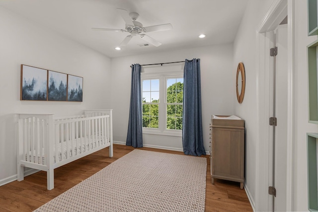 bedroom with wood finished floors, baseboards, a ceiling fan, recessed lighting, and a crib