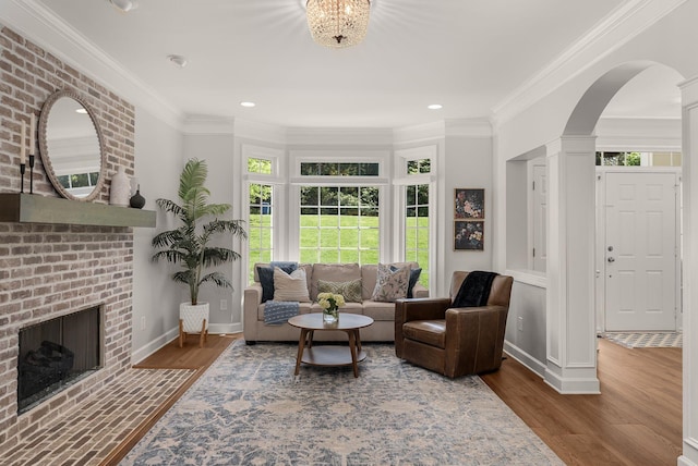 living area featuring healthy amount of natural light, wood finished floors, a fireplace, baseboards, and crown molding