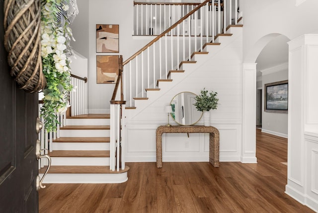 stairs with wood finished floors, arched walkways, ornamental molding, and baseboards