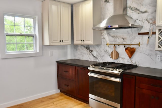 kitchen with wall chimney exhaust hood, stainless steel range with gas stovetop, decorative backsplash, dark countertops, and baseboards