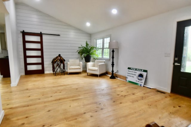 living area featuring a barn door, wood finished floors, vaulted ceiling, recessed lighting, and wooden walls