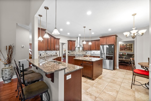 kitchen featuring stainless steel fridge, a sink, wall chimney range hood, tasteful backsplash, and a center island