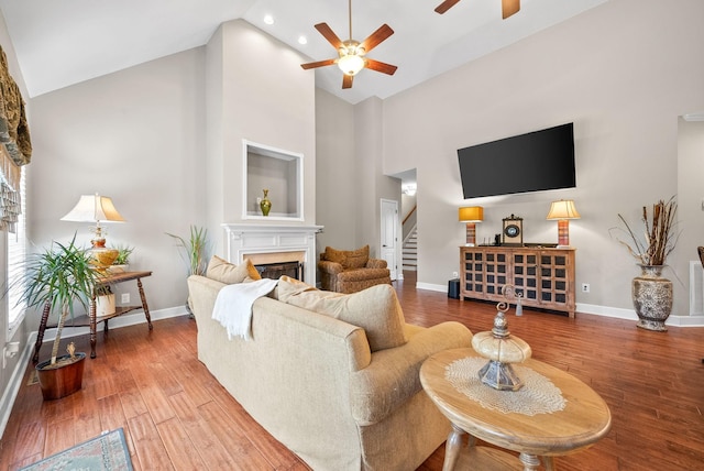 living area with a high end fireplace, high vaulted ceiling, stairs, ceiling fan, and wood finished floors