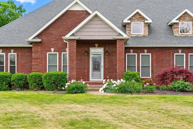 view of front of property featuring a front yard, brick siding, and a shingled roof