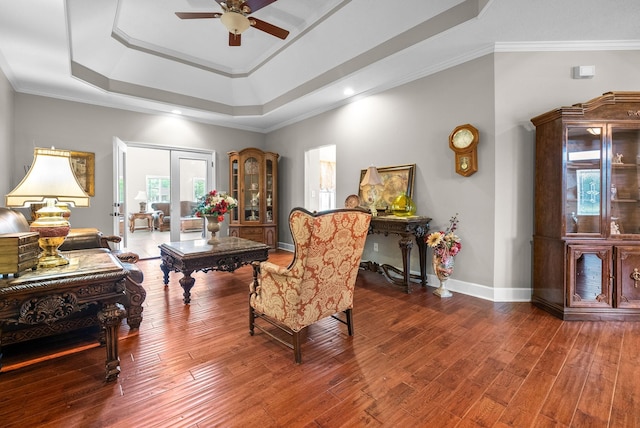 living room featuring ceiling fan, wood finished floors, a tray ceiling, baseboards, and ornamental molding