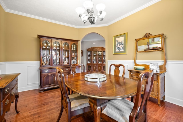 dining room with arched walkways, a chandelier, wood finished floors, a wainscoted wall, and crown molding