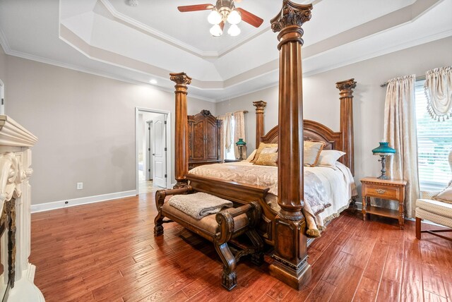 bedroom with a tray ceiling, decorative columns, wood-type flooring, crown molding, and baseboards