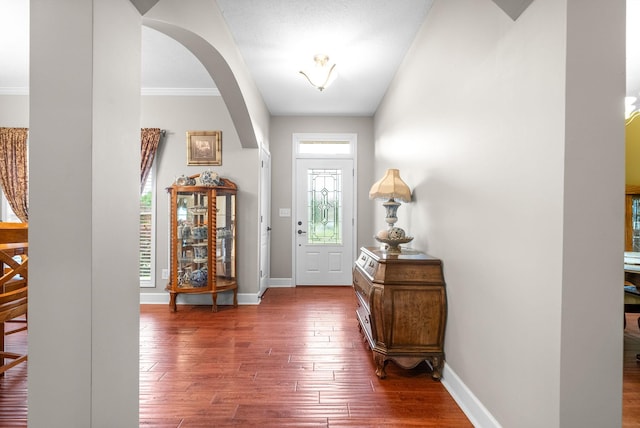 entrance foyer featuring dark wood-style floors, arched walkways, baseboards, and crown molding