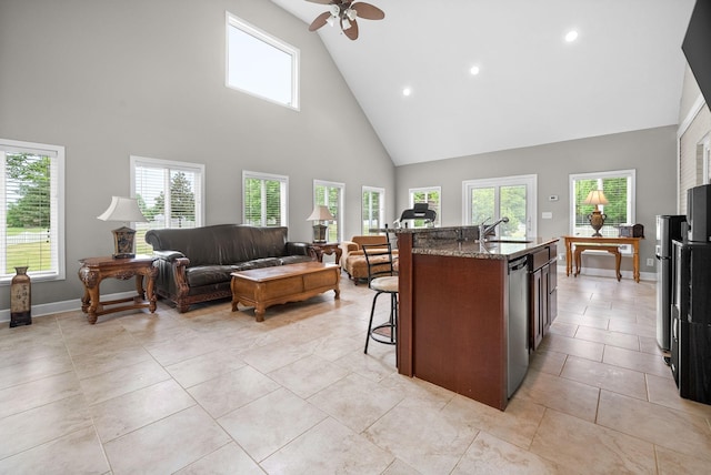kitchen featuring a breakfast bar area, high vaulted ceiling, dark stone counters, ceiling fan, and a sink