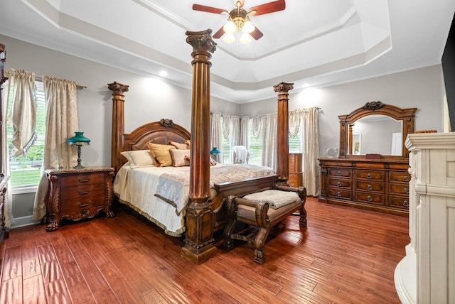 bedroom featuring a raised ceiling, decorative columns, wood-type flooring, ornamental molding, and ceiling fan