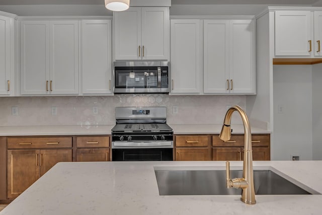 kitchen featuring appliances with stainless steel finishes, a sink, tasteful backsplash, and white cabinets