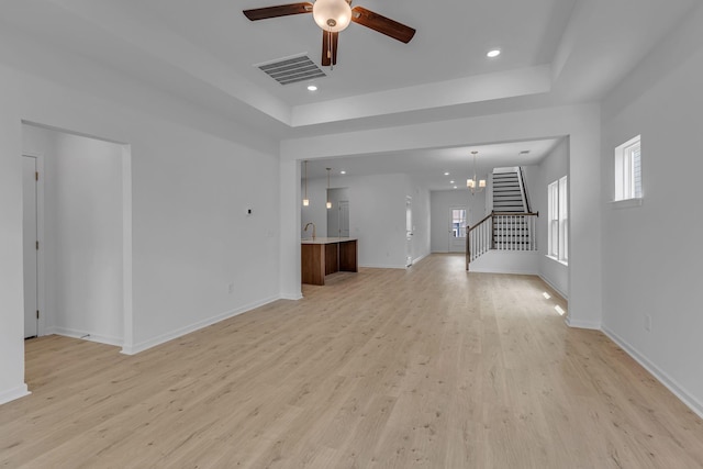 unfurnished living room featuring light wood finished floors, a tray ceiling, a ceiling fan, recessed lighting, and baseboards