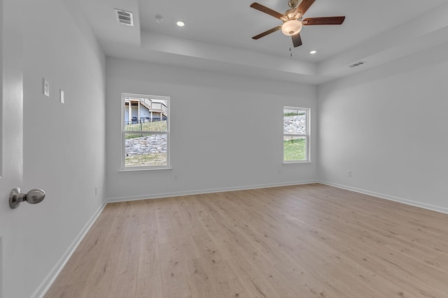 empty room featuring light wood-style floors, a tray ceiling, recessed lighting, ceiling fan, and baseboards