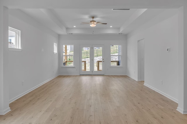 unfurnished living room featuring a raised ceiling, a ceiling fan, light wood-type flooring, recessed lighting, and baseboards