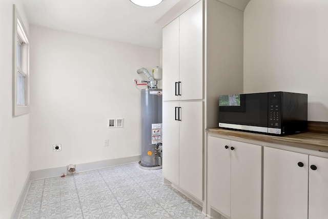 laundry area featuring water heater, electric dryer hookup, baseboards, and cabinet space