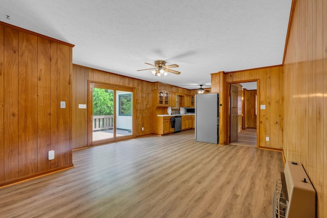unfurnished living room featuring a ceiling fan, wooden walls, light wood-style floors, baseboards, and a textured ceiling