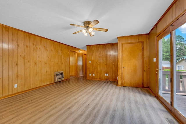 empty room featuring heating unit, light wood-style floors, wooden walls, a ceiling fan, and ornamental molding