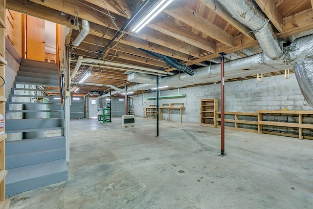 unfinished basement featuring stairs and concrete block wall