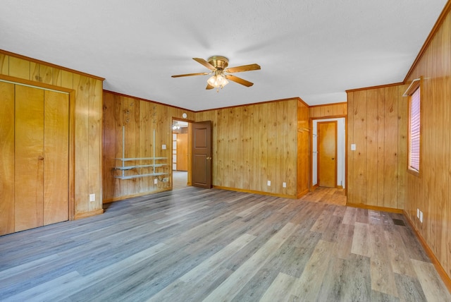 unfurnished bedroom featuring wood finished floors, wooden walls, crown molding, baseboards, and a ceiling fan