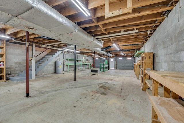 unfinished basement with water heater, stairs, and concrete block wall