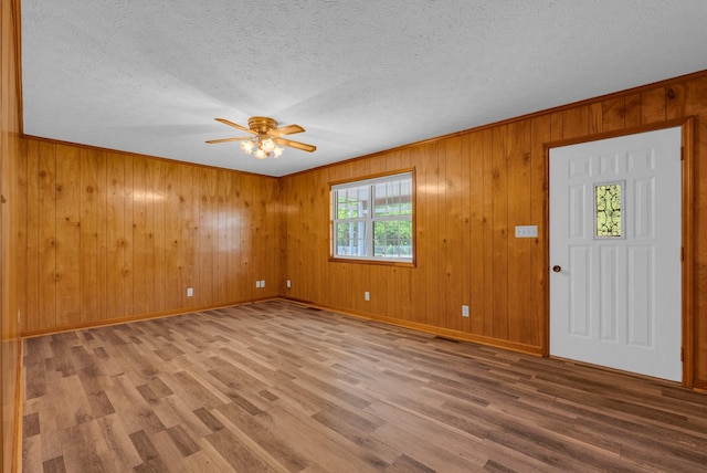 entryway with ceiling fan, wood finished floors, baseboards, a textured ceiling, and wooden walls