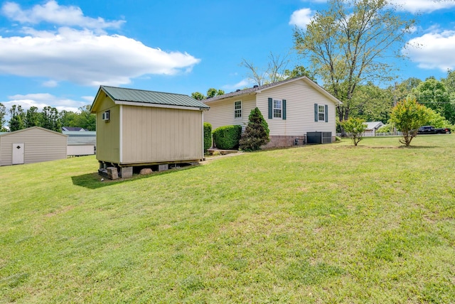 rear view of property with a storage shed, an outdoor structure, central AC, and a yard