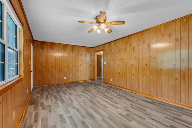 unfurnished room featuring wood finished floors, a ceiling fan, wooden walls, and baseboards
