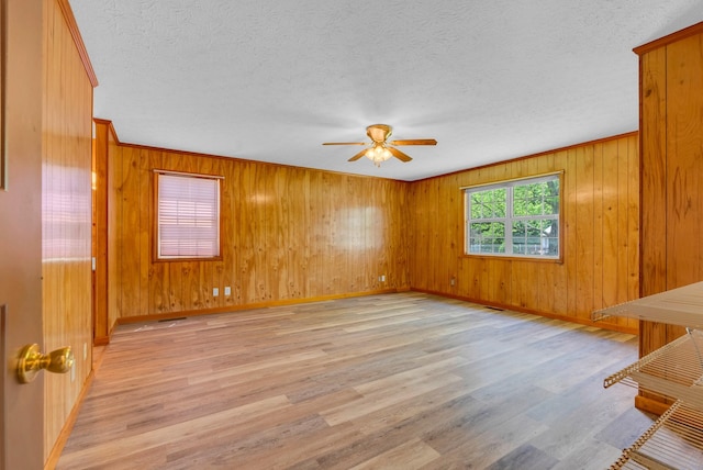 empty room with ceiling fan, baseboards, light wood-style floors, a textured ceiling, and wood walls