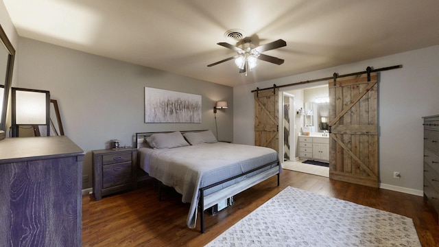 bedroom featuring a barn door, dark wood finished floors, baseboards, ceiling fan, and ensuite bathroom