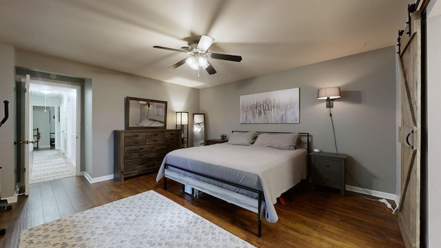bedroom with a barn door, wood finished floors, baseboards, and a ceiling fan