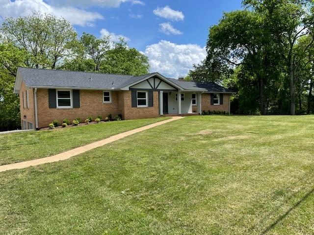 ranch-style home featuring brick siding, a front yard, and covered porch
