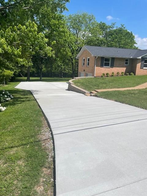 view of front of house with concrete driveway, brick siding, a garage, and a front lawn