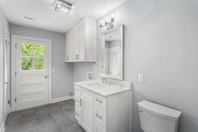 bathroom featuring baseboards, vanity, toilet, and stone finish floors