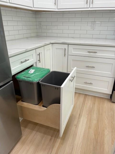 kitchen view of freestanding refrigerator, light wood-type flooring, and white cabinetry