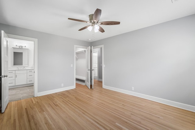 unfurnished bedroom with baseboards, light wood-style flooring, ensuite bathroom, a spacious closet, and a closet