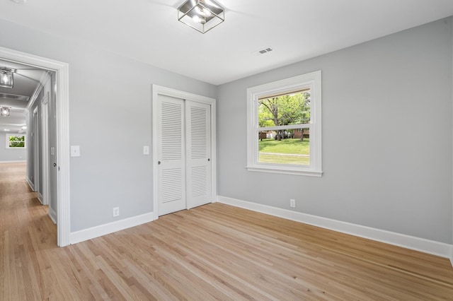 unfurnished bedroom with baseboards, a closet, light wood-type flooring, and attic access