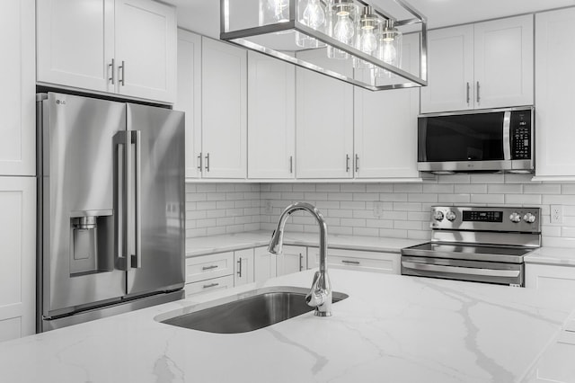 kitchen with stainless steel appliances, a sink, white cabinetry, backsplash, and light stone countertops