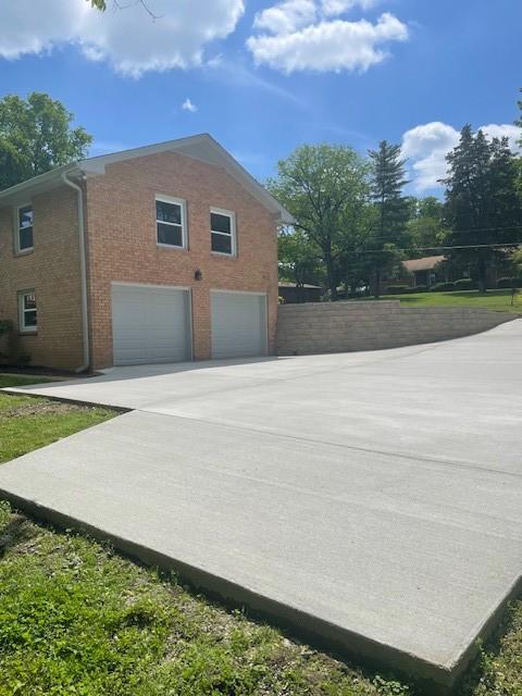 view of side of home featuring a garage, concrete driveway, brick siding, and fence