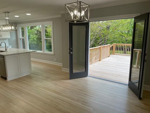 unfurnished dining area with baseboards, a chandelier, ornamental molding, light wood-style flooring, and a sink